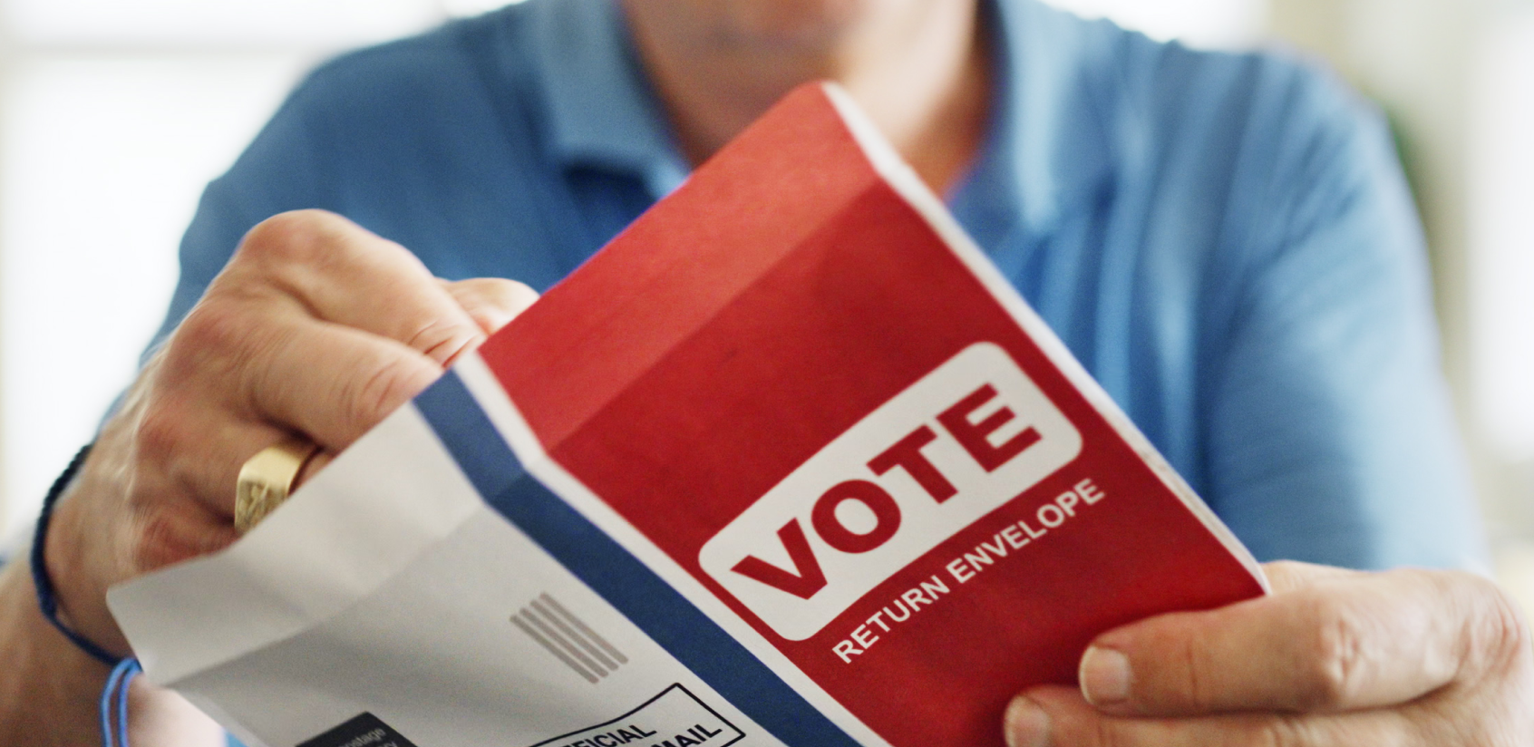 Close up of a hand putting a mail ballot into a return envelope that says “vote” on front.