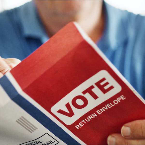Close up of a hand putting a mail ballot into a return envelope that says “vote” on front.