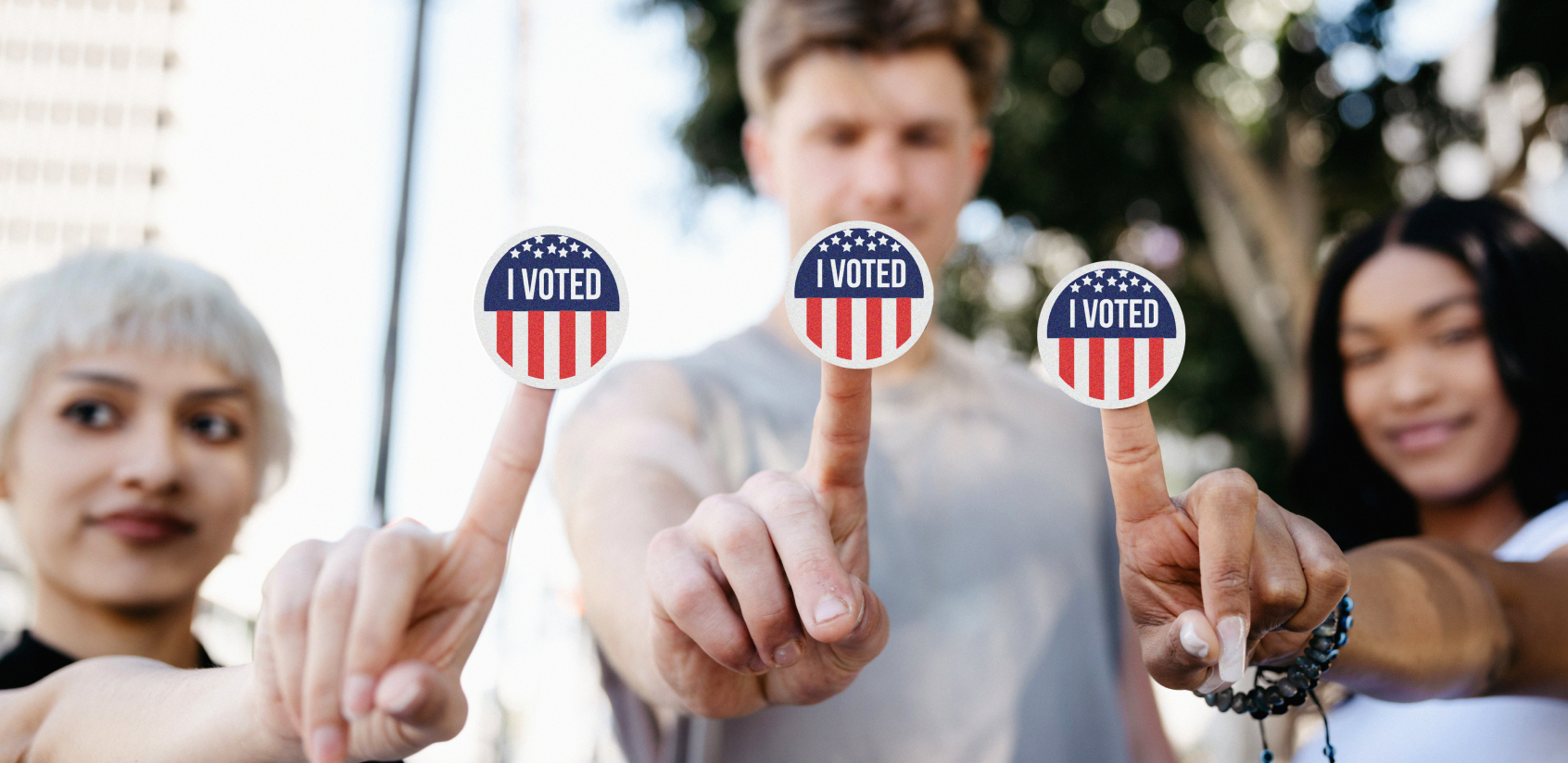 Two women and a man holding out an “I Voted” sticker on the tip of each of their fingers.