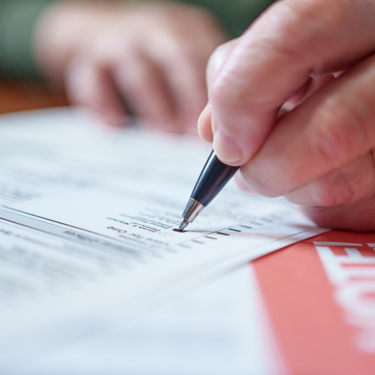 Close-up image of a hand holding a pen while filling out a mail-in ballot.